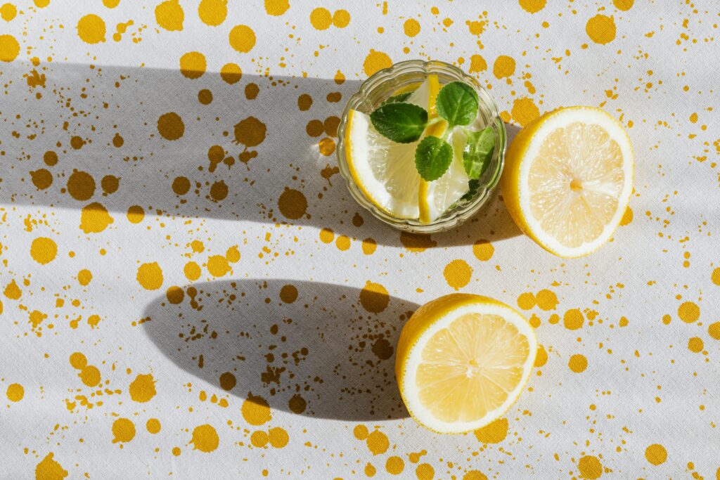 pexels-photo-4021872-4021872 Top view of glass of fresh cold drink with halves of lemon on table with white tablecloth in yellow blots