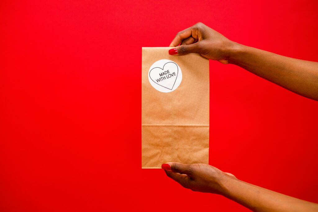 Brown paper bag with 'Made With Love' label held by hands over a red background.